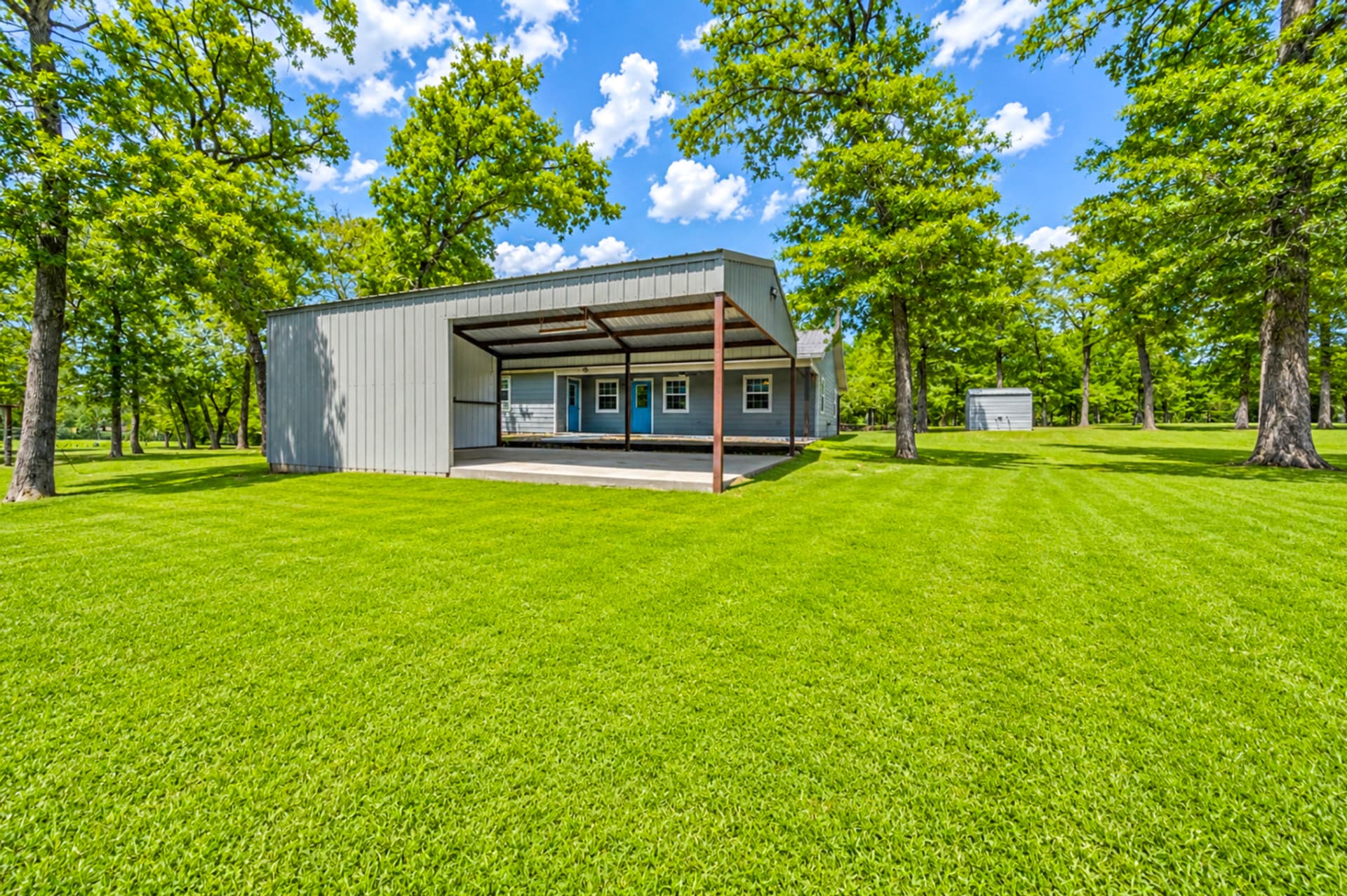 Open-sided pole barn with concrete slab facing the home's covered porch