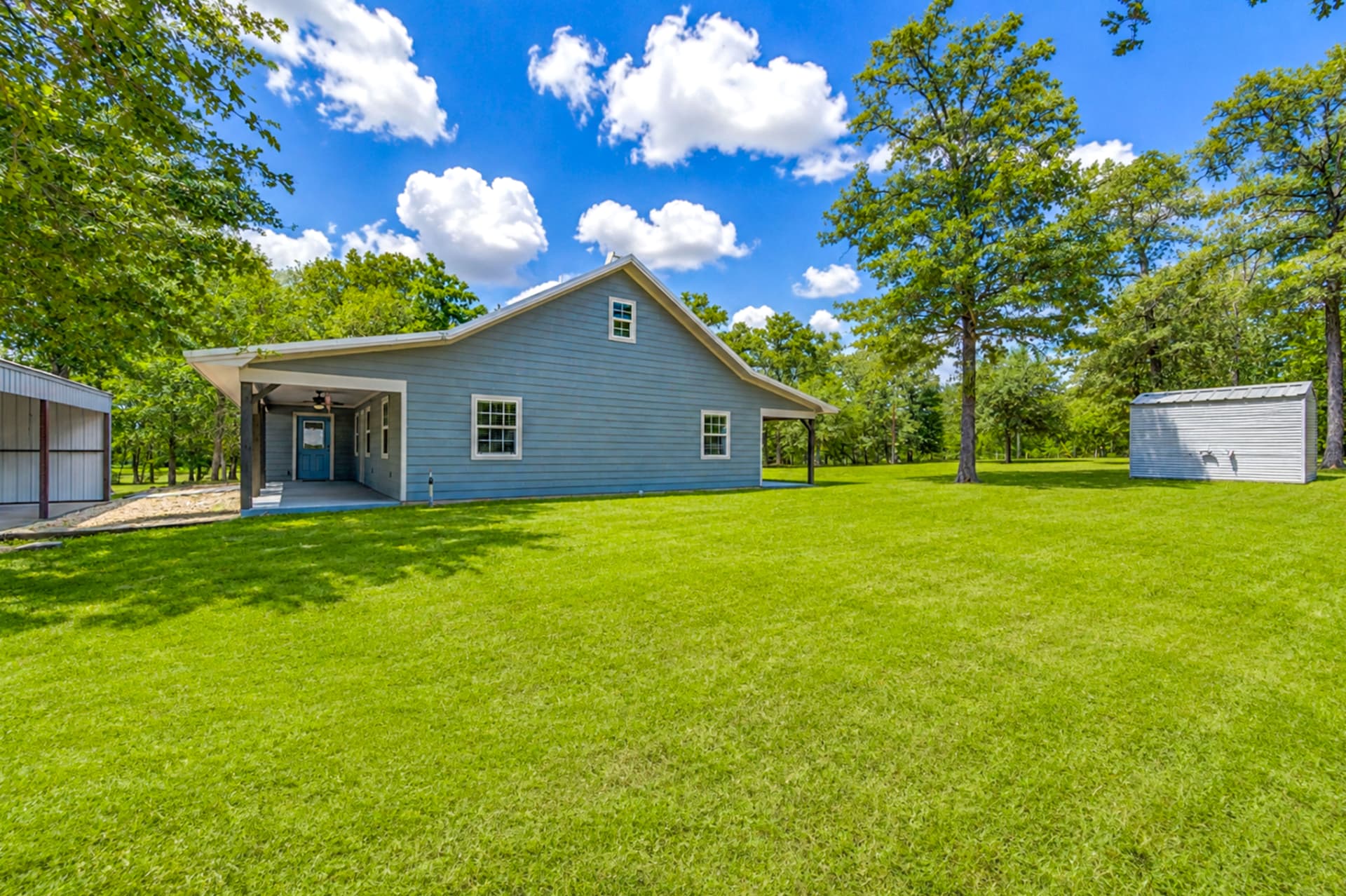Side view of the farmhouse with covered porch, storage shed, and shaded lawn