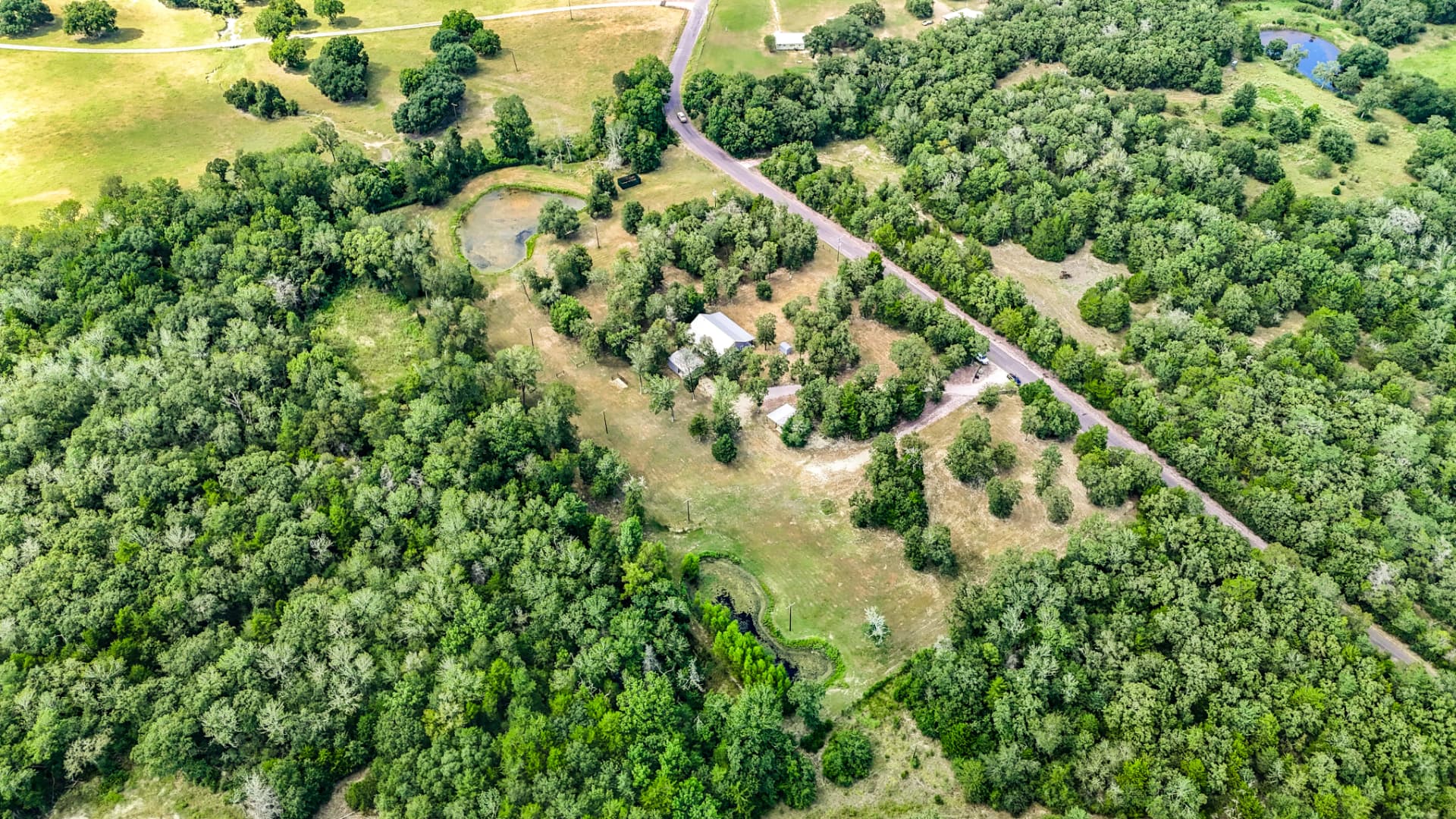 Aerial view of the farmhouse, pole barn, and stock pond framed by oaks